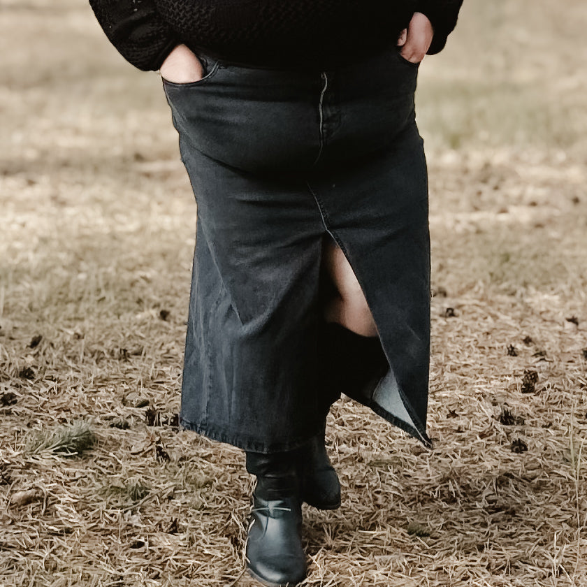 Plus size woman wearing a trendy and comfortable belted black denim midi skirt with a front slit 